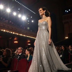Torrey DeVitto, at the Gotham Awards, wearing a floor-length silver sequined gown. Crowded auditorium, spotlight on her