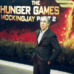 Jon Kilik, Caucasian man with receding hairline, in a tailored suit. Posing formally at a film premiere. Promotional backdrop for 'The Hunger Games: Mockingjay Part 2' behind him.