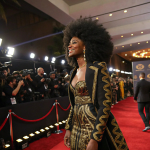 Nomalanga Shozi at the Black Girls Rock awards. Wearing a black and gold outfit, large afro hairstyle. Crowded stage with red carpet and flashing cameras