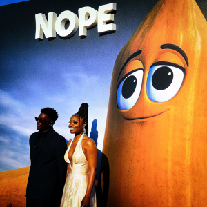 Keke Palmer, with braided hairstyle, and Daniel Kaluuya, in black suit and sunglasses, at 'Nope' premiere. Large red friendly character backdrop