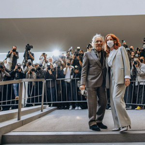 Abel Ferrara and Shanyn Leigh at the New York Film Festival premiere. Dressed in formal attire, they pose for photographers against a sea of flashing cameras and curious onlookers.