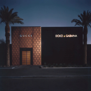 Sophisticated storefronts of Gucci and Dolce & Gabbana at The Crystals mall in Las Vegas. Angular facade with gold logo. Palm trees and blue sky backdrop.