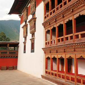 A majestic temple complex, the Paro Dzong, features a pristine white exterior adorned with intricate wooden carvings. Surrounded by a serene courtyard and additional architectural elements.