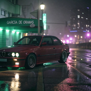 Dark cityscape at night. A shiny red BMW M3 E30 Evolution II parked on a wet street. Soft headlights glow on the pavement. Blurred green and purple lights from distant buildings. Sign reads GARCIA DE ORAMAS