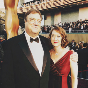 John Goodman and Annabeth Hartzog at the Academy Awards. John in a black tuxedo, Annabeth in a red gown.