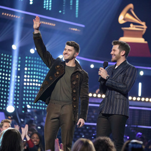 Nick Jonas and Andrew Taggart on stage at the Grammy Awards, celebrating with applause and cheers from the audience. Lavish stage setup with LED screens and bright lights.