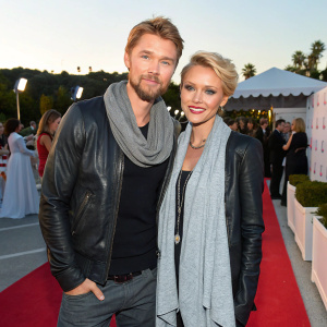 Chad Michael Murray and Nicky Whelan at a fashion gala. They both wear casual chic outfits. Murray in a scarf and black shirt, Whelan in a gray scarf and leather jacket. Event is outdoors with a festive atmosphere