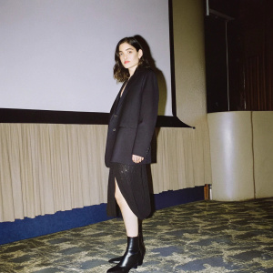 Pegah Ferydoni attending the 'Bad Boys For Life' premiere in Berlin. Wearing black blazer and skirt, black boots. Standing alone in an empty, dimly lit room.