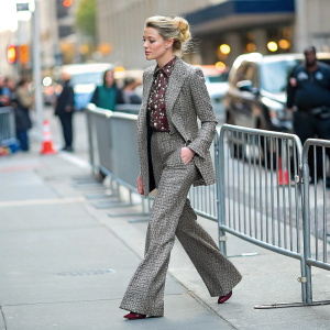 Amber Heard, walking on a busy city street, blonde updo, grey and brown patterned suit with wide-legged pants and patterned blouse. Metal barrier and blurred cityscape background