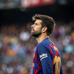 Gerard Pique, focused gaze, wearing Barcelona FC jersey. Crowded stadium background blurred.