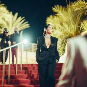 Shay Mitchell at the Cannes Film Festival premiere. Wearing a black suit and diamond choker. Starlit night, red carpet