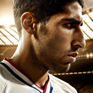 Close-up of Achraf Hakimi. Focused face. Wearing the official jersey of Paris Saint-Germain. Blurred stadium background