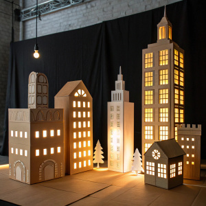 Cardboard cityscape, miniature structures, shadow play. Brightly lit on black backdrop, artistic concept.