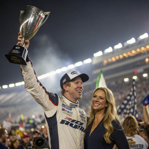 Brad Keselowski and Paige White, both Caucasian, celebrating their NASCAR victory. Crowded stadium background