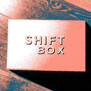 Modern sleek Shift Box logo, silver, placed against a rough wooden background.