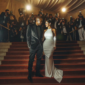 Kanye West and Kim Kardashian at a glamorous gala. Kanye is in a sleek black suit, Kim is in a stunning white gown. The backdrop is filled with paparazzi and fans.