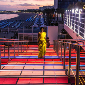 Radhika Apte, elegant in a yellow saree, poses at the Cannes Film Festival. Crowded beach backdrop.