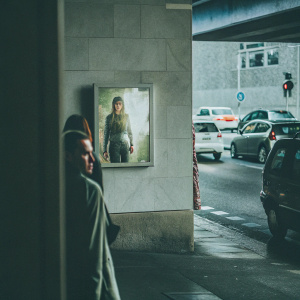 Realistic photo of a movie poster for 'Maze Runner: The Death Cure'. The poster is prominently displayed on a wall near a bustling city street with parked cars and pedestrians passing by.