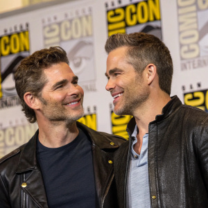 Eric Bana and Chris Pine attending Comic-Con in San Diego. Eric with wavy hair and stubble, wearing black leather jacket. Chris with short haircut, dressed casually yet stylishly. Both actors are smiling and interacting closely.