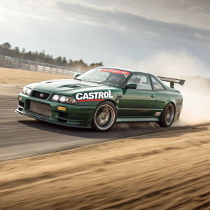 A sleek Nissan Skyline GT-R in green racing livery, sponsored by Castrol. On a dusty track during a high-speed race.