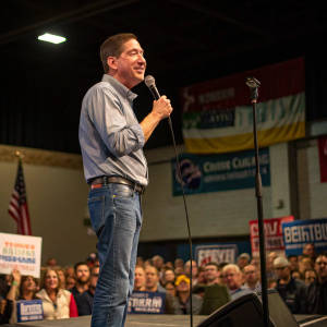 Glenn Greenwald, dressed in a casual shirt and jeans, speaking at a political rally.