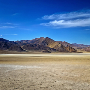 a fresh lake with shores of green lawns, palm-clad mountains in the background, and behind them a blue sky