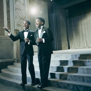 Tyler James Williams and Jacob Latimore on the stage at the NAACP Image Awards. Wearing black tuxedos and grinning broadly.