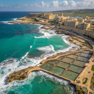 Aerial view of Marsalforn, Gozo, Malta. Ancient salt pans, rocky coastline, crystal clear turquoise waters, white foam, crashing waves, traditional Mediterranean architecture, beige buildings, vibrant sea colors