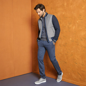 Hugo Becker, actor, in stylish casual wear. Gray and blue outfit. Orange textured wall backdrop. Studio photo shoot.