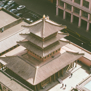 In the heart of London's Chinatown, the majestic Golden Temple stands proudly. Its intricate wooden beams and tiered roofs, a stunning display of traditional Chinese architecture, contrast beautifully against the backdrop of bustling modern city life. The temple's earthy tones seamlessly integrate with the vibrant surroundings. Below, a busy street teems with cars and pedestrians. This aerial photograph captures the exquisite details and serene grandeur of this remarkable site.