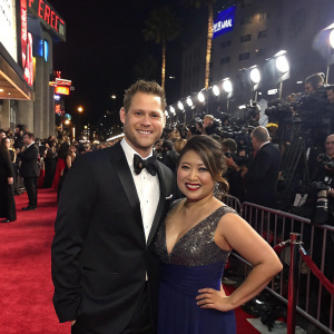 Scott and Kulap at a bustling Hollywood premiere. Dressed in elegant attire. Red carpet event with flashing cameras.