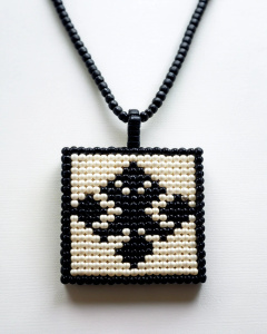 Peyote stitch beaded rectangular necklace. On it there is the picture of a kanji. The kanji is black on a white surface.