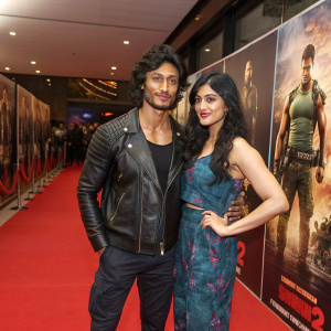 Vidyut Jammwal and Adah Sharma at the premiere of Commando 2. They are standing on a vibrant red carpet, flanked by the movie's promotional banners depicting intense action sequences.