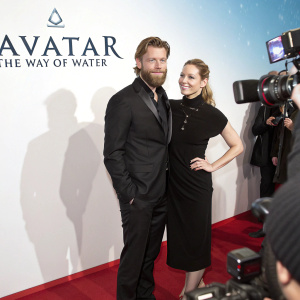 Ken Duken and Marisa Leonie Bach at Berlinale film festival. Ken Duken, wearing a black suit, with a beard. Marisa Leonie Bach, in a stylish black dress. They are standing in front of a white backdrop with 'Avatar - The Way of Water' title. Red carpet event with flashing cameras.