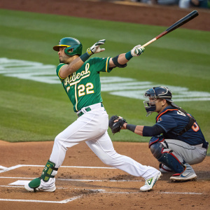 Ramón Laureano, number 22, in green jersey, stepping into batting stance. Focused expression, dynamic pose. Catcher crouched behind him. Green grass field visible
