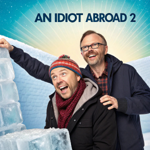 Promotional poster for 'An Idiot Abroad 2'. Ricky Gervais and Stephen Merchant standing next to a man trapped in a block of ice, Karl Pilkington. Bright and colorful background.