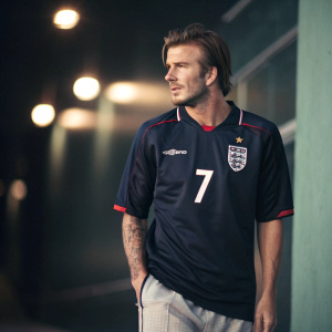 David Beckham in a candid shot. Wearing number 7 jersey with England's emblem. Dark background, soft lighting