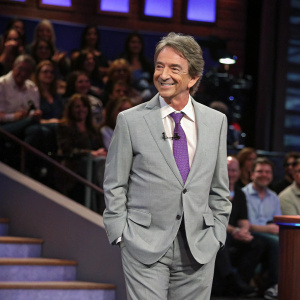 Martin Short in a light grey suit and a purple tie, appearing on a talk show. Studio audience visible behind