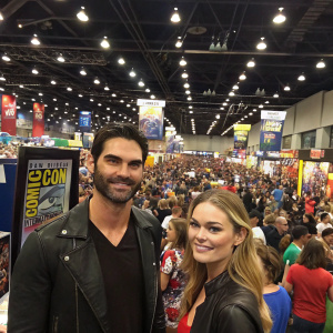 Tyler Hoechlin and Shelley Hennig attending a bustling comic-con convention. Crowded hall with enthusiastic fans and numerous comic book displays.