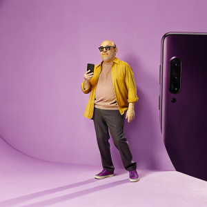 Willie Garson at a tech expo. Bald head, wearing black sunglasses. Casual outfit. Surrounded by Samsung branded backdrop.