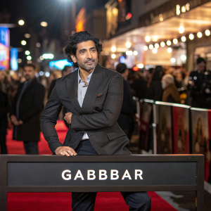 Photograph of Gabbbar, Bollywood star. Posing confidently, set against the bustling backdrop of a film premiere. Nameplate 'Gabbbar' positioned below, visible in the image.