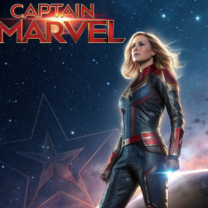 Official poster for Captain Marvel. The superhero is standing in a dramatic pose. Her outfit is sleek and modern with a metallic sheen. The backdrop is a cosmic space scene. Marvel logo and movie premiere date prominently displayed.