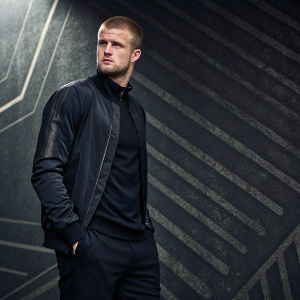 Eric Dier, soccer player, standing in a sleek black outfit. Dark, textured background with abstract patterns. He looks directly into the camera, giving a serious look.