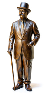 A bronze statue of Hercule Poirot as played by David Suchet, a bowler hat on his head, fine mustache, with a walking cane, left hand placed behind his back