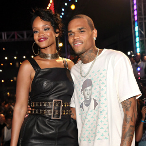 Rihanna and Chris Brown at the music awards show. Rihanna in a black leather dress with a belt. Chris Brown in a white graphic tee. Flashing lights and crowd in the background.