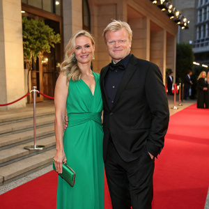 Oliver Kahn and Svenja at a gala event. Svenja in a vibrant green dress, Kahn in a black suit. They pose elegantly on the red carpet.