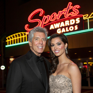 Michael Buffer and Christine Prado attending the Sports Awards Gala, posing in front of a neon sign.