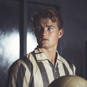 Caucasian male footballer Matthijs De Ligt in a studio setting. Wearing Juventus jersey. Intense gaze, sharp focus. Dark blurred background.