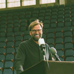 Jurgen Klopp, grinning widely with teeth showing, beard, glasses, during a Premier League press conference.