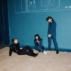 A diverse group of characters from 'Bionic Island', each in unique poses, wearing sleek, futuristic attire. The set features a minimalist, tech-filled backdrop with holographic elements. The floor is covered in a plush rug.